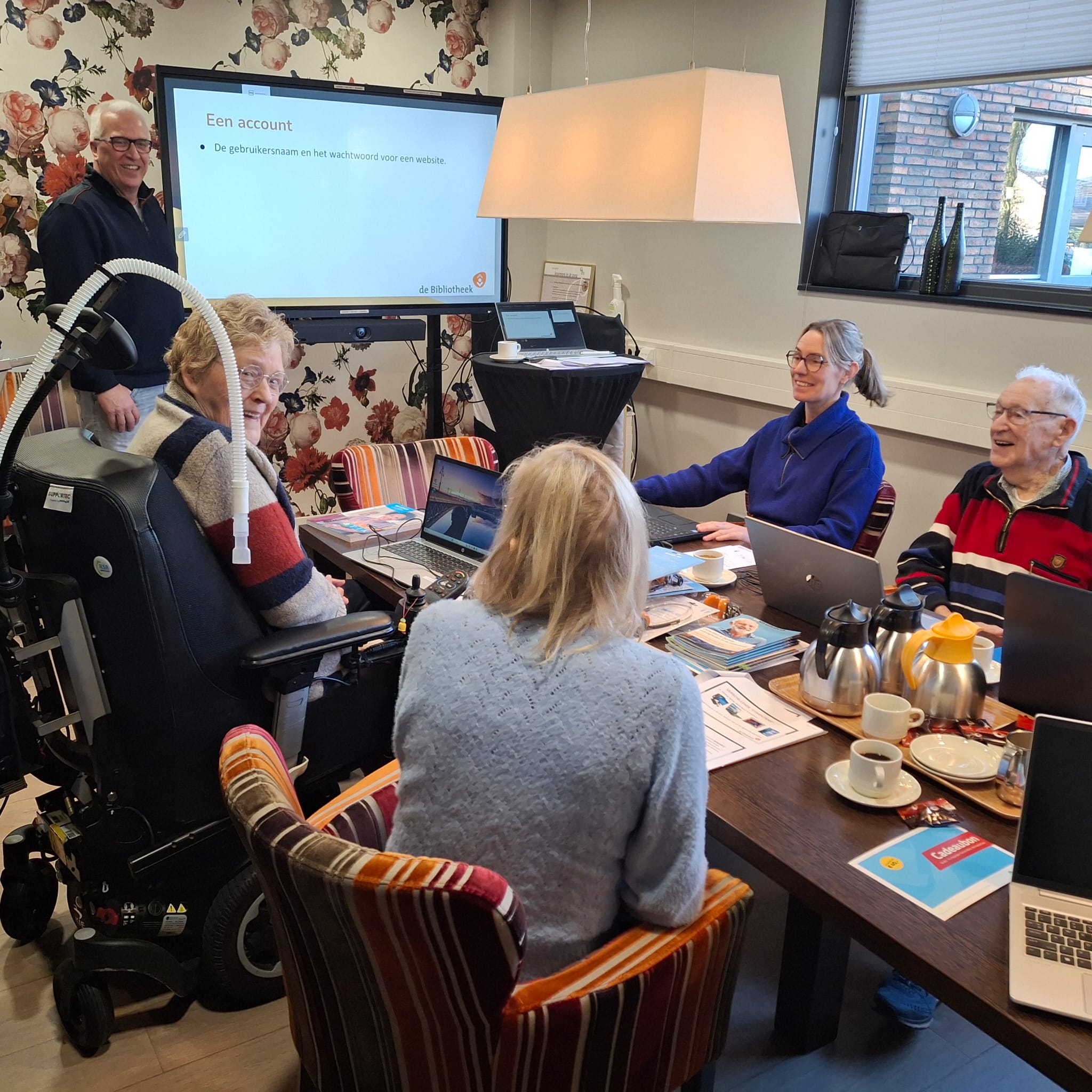 Medewerker van de bibliotheek zit met 3 deelnemers van een cursus aan tafel. Ze hebben allemaal een laptop voor zich.