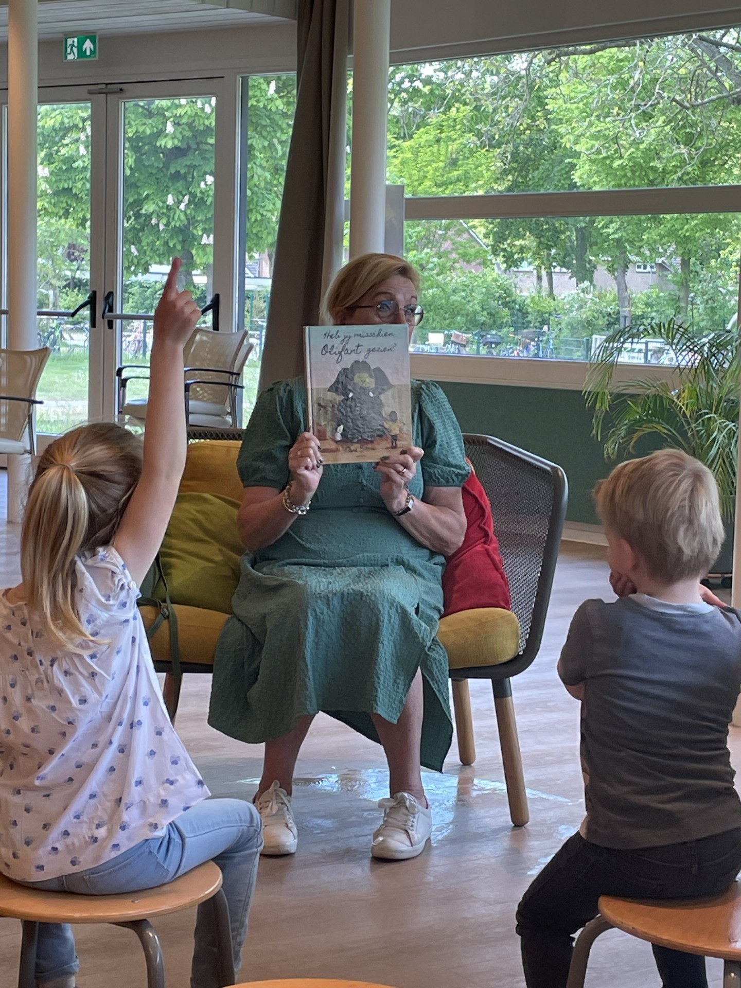 Twee kinderen luisteren naar een vrijwilliger die vertelt over het boek 'Heb jij misschien Olifant gezien'. 