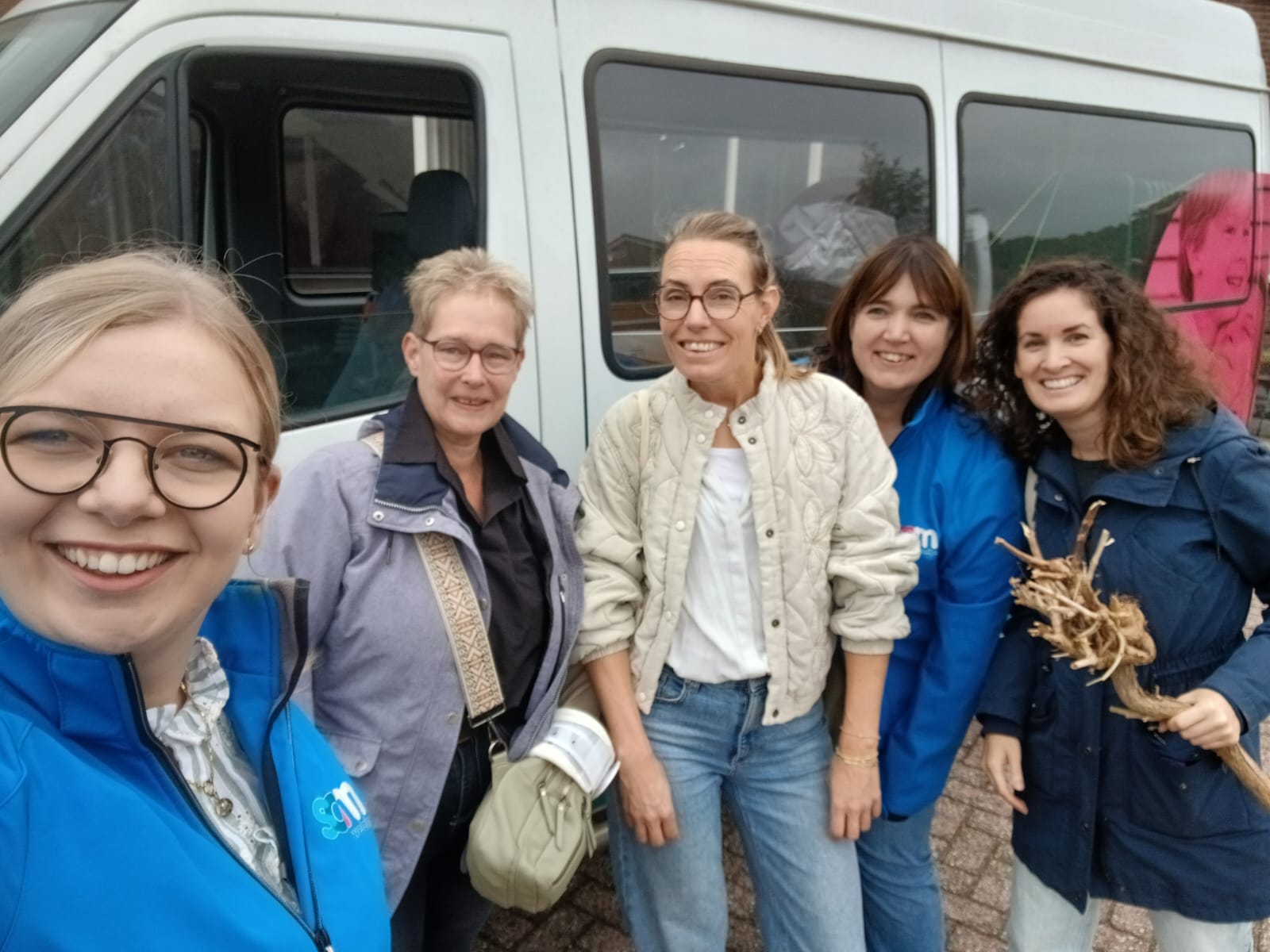 Medewerkers van de Bibliotheek en Saam Welzijn staan lachend voor een bus. 