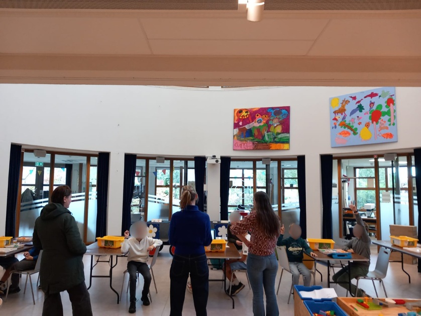Twee medewerkers van de bibliotheek staat voor een groep kinderen uit te leggen