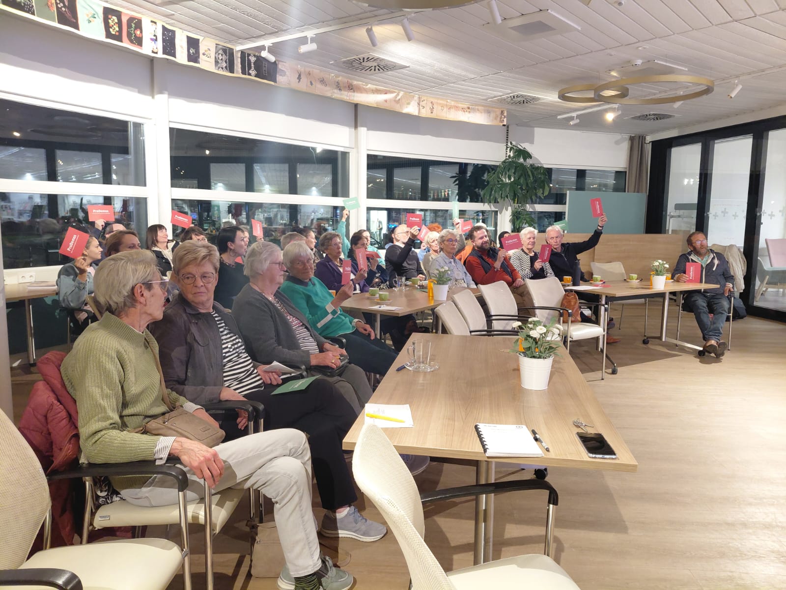 Mensen zitten allemaal in een zaal en een aantal houd een rode kaart omhoog.