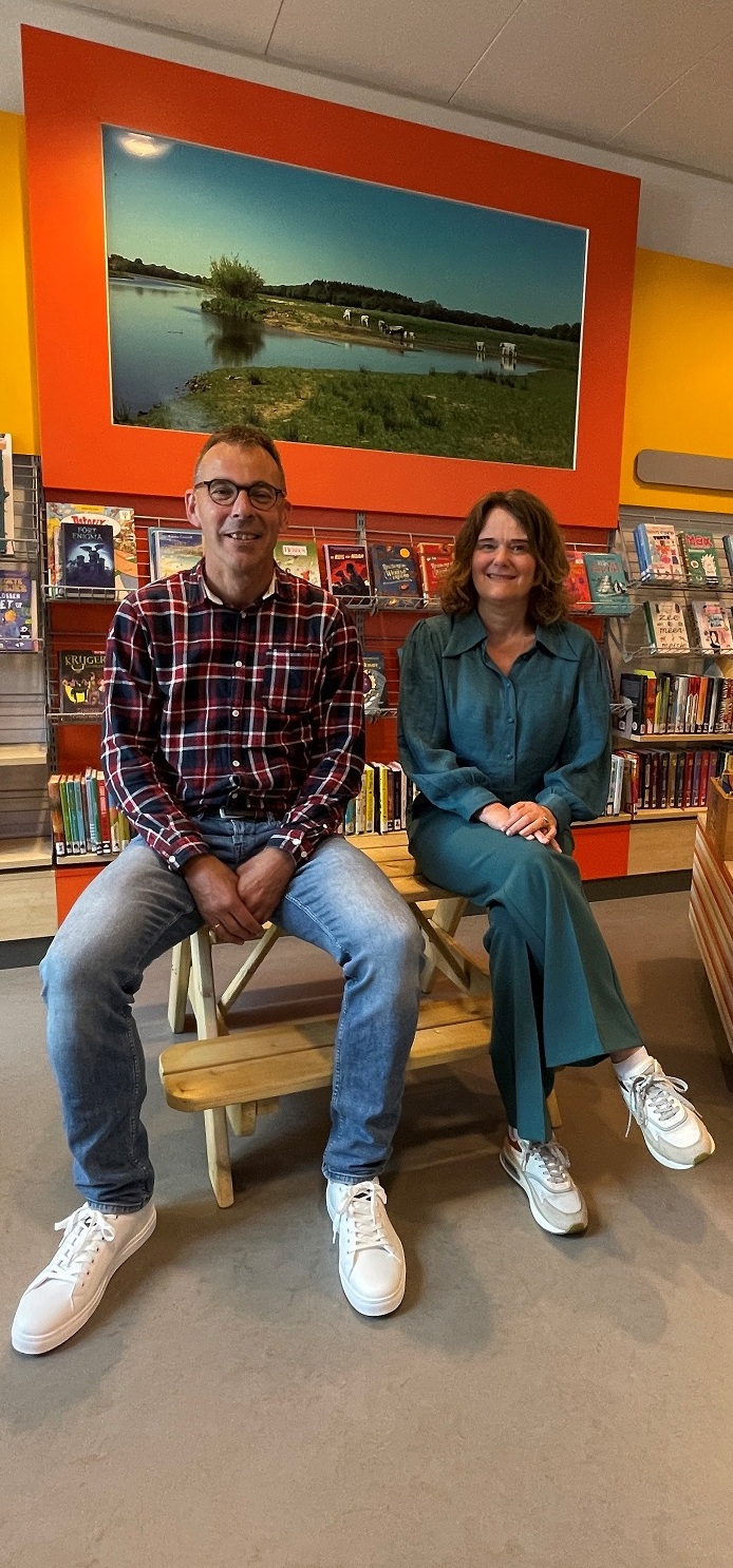 De voorzitter en de directeur zitten op een bankje in Bibliotheek Oudleusen.