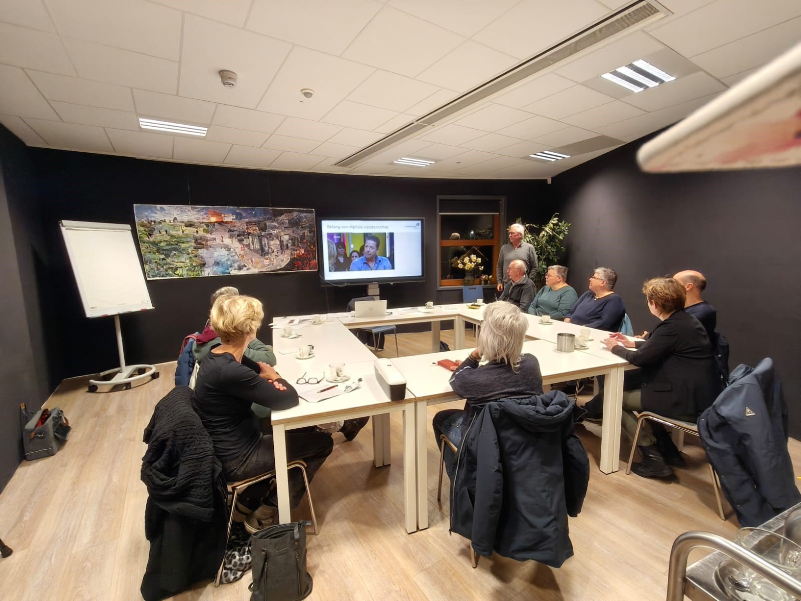 Deelnemers van de cursus zitten in een ronde opstelling en kijken naar een scherm.