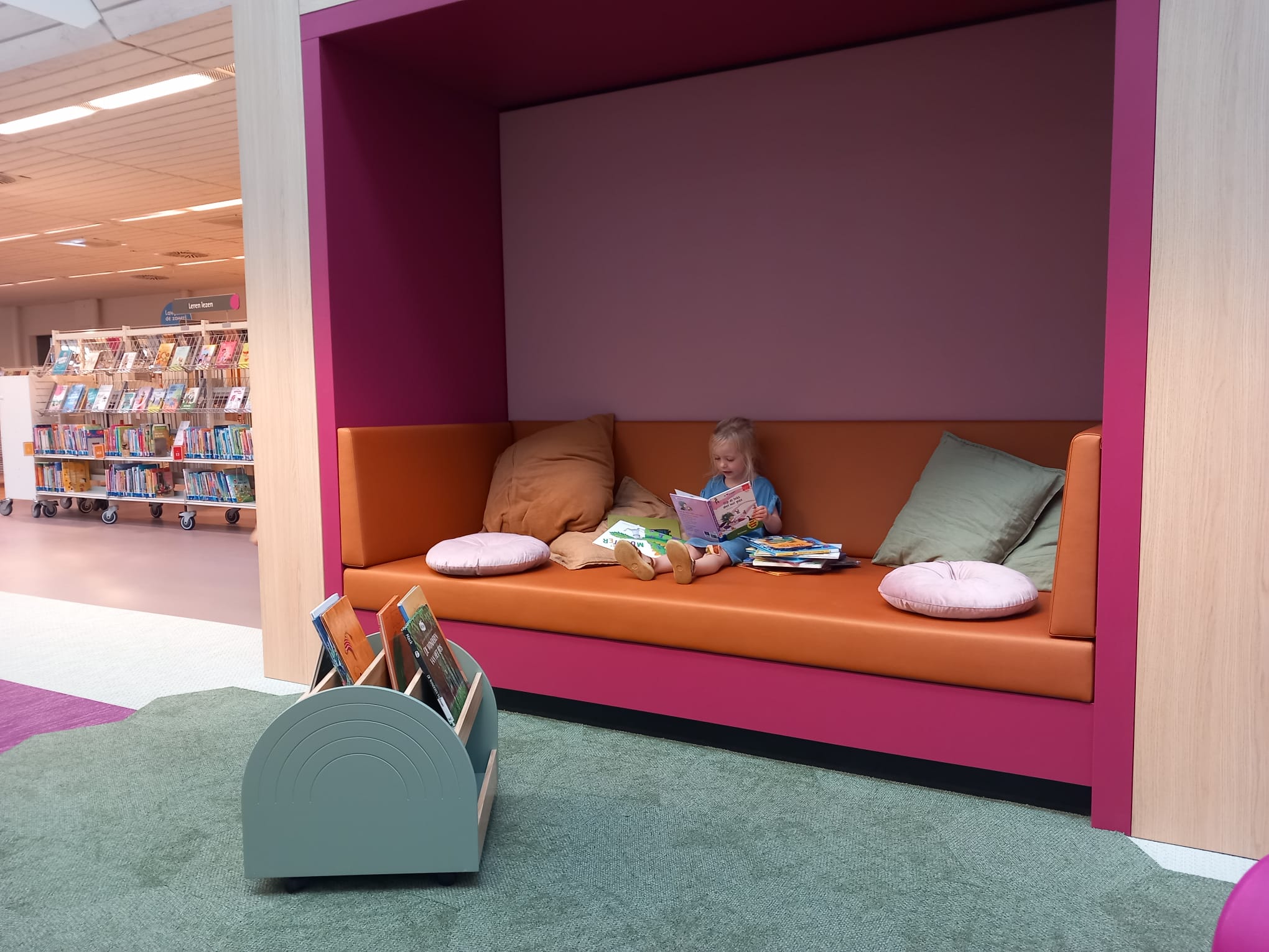 Meisje zit op een bank te te lezen met een stapel boeken ernaast in Bibliotheek Dalfsen.