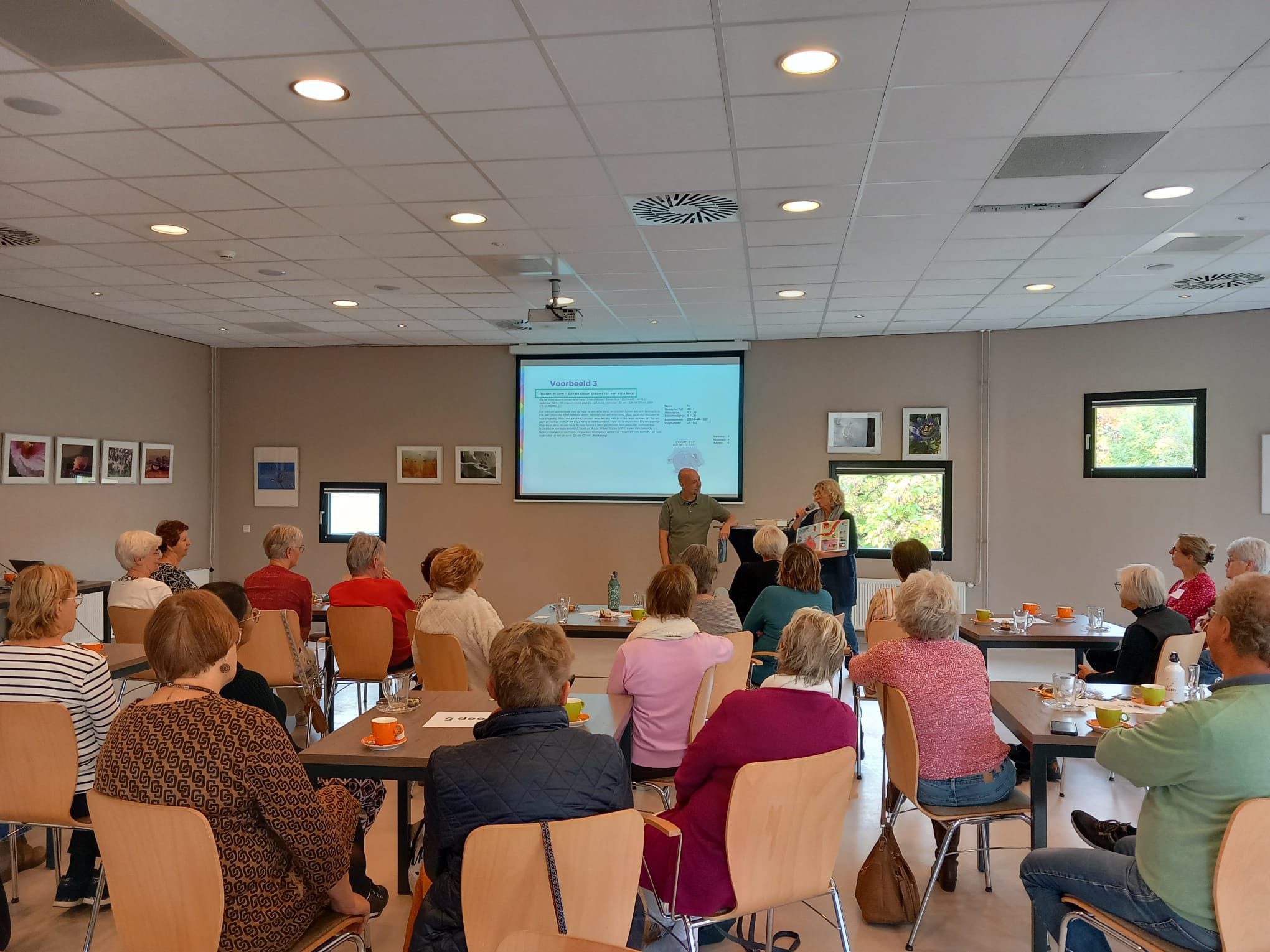 Vrijwilligers zitten op een stoel te luisteren naar twee sprekers.