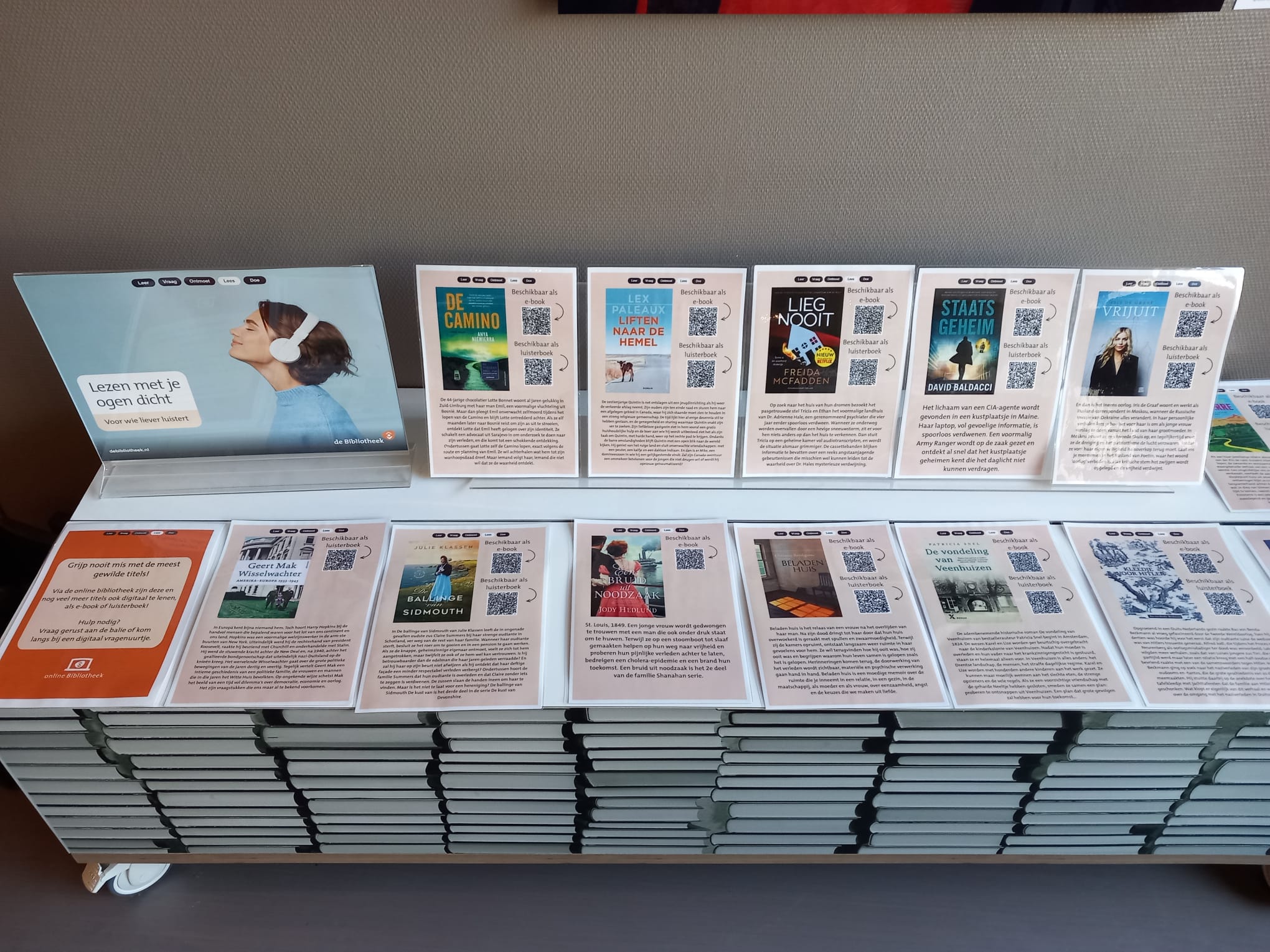 Tafel met daarop a4 tjes waarop de voorkant van een boek is te zien met een qr code ernaast.
