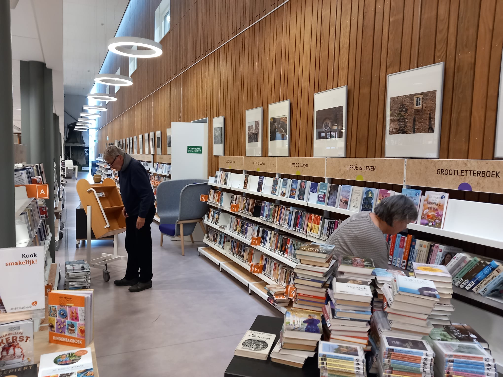 Twee vrijwilligers zijn bezig met het verplaatsen van boeken in kasten in Bibliotheek Nieuwleusen.
