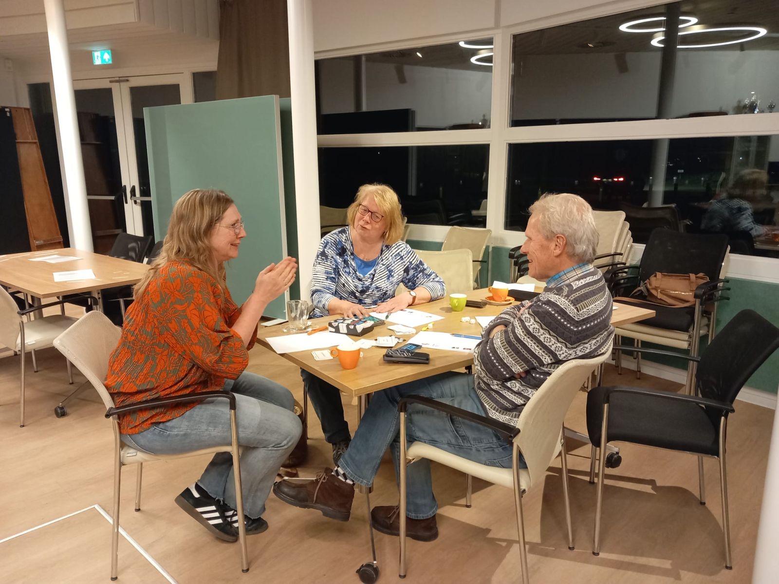 3 mensen overleggen aan een tafel vol met papier en 3 kopjes koffie.