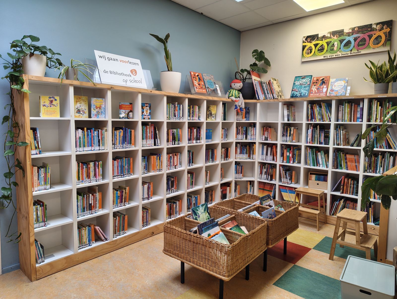 Kasten en manden met kinderboeken, vrolijk aangekleed met planten en knuffels.