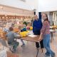 Twee medewerkers van de bibliotheek staan lachend bij een tafel terwijl kinderen druk bezig zijn met lego ontwerpen