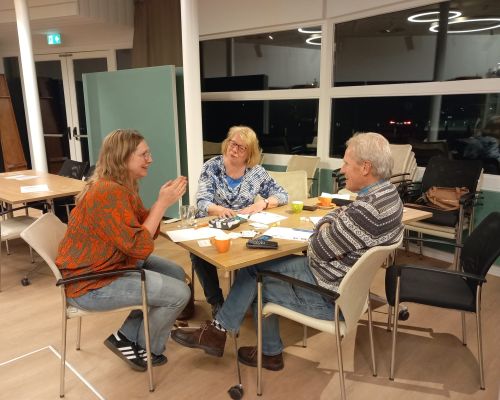 3 mensen praten met elkaar, zittend aan een tafel die vol ligt met papier